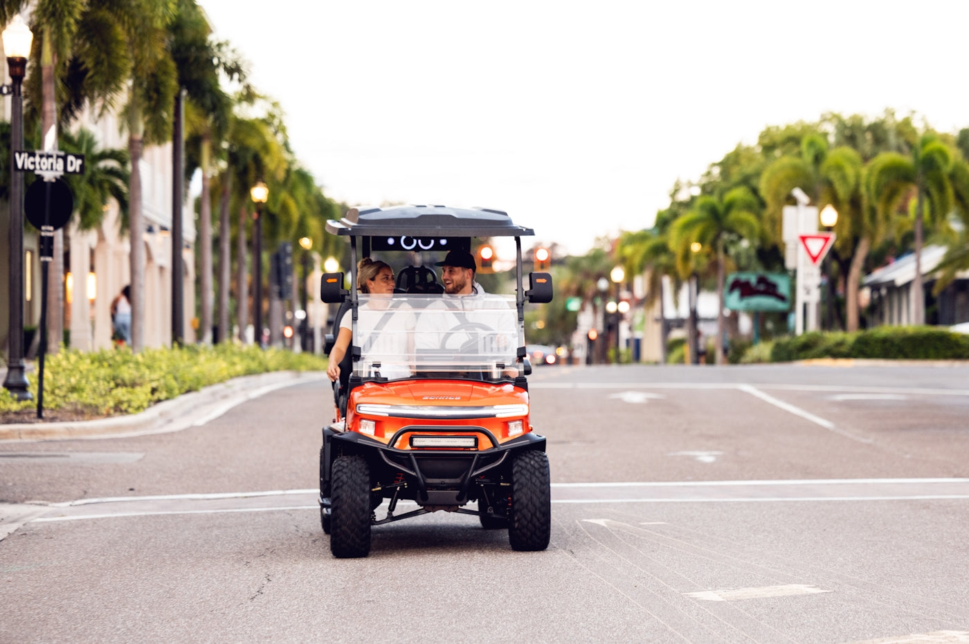 Two people driving a golf cart down a street