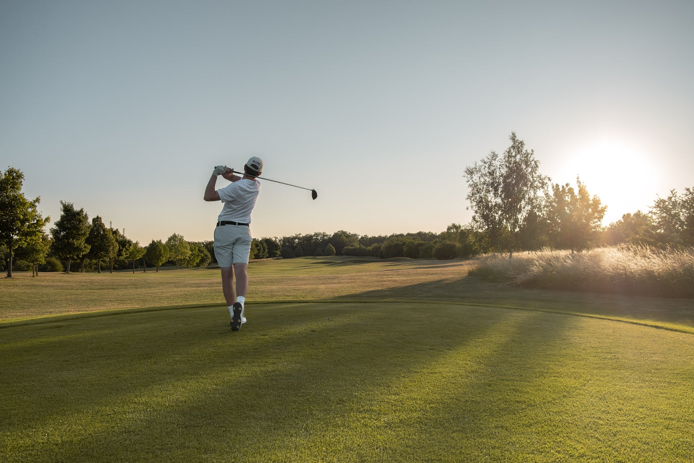 A golfer swings on a sunny, open course.